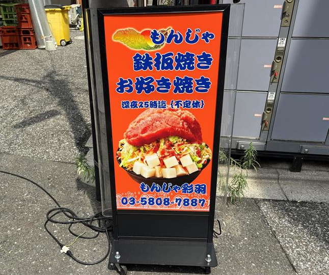鉄板の上でもんじゃが焼ける湯気越しに、木のテーブル席が奥まで続く店内